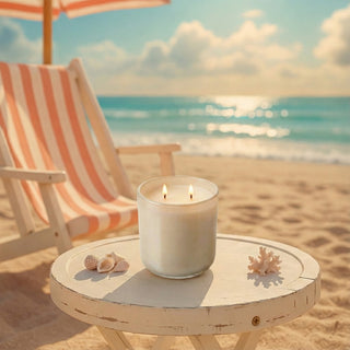 Beachside Dream – Staycation beach-inspired premium coconut apricot wax candle lit with dual flames, glowing softly on rustic white table with seashells & coral, tropical beach sunset scene with striped lounger & ocean waves