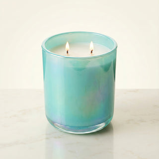 Shimmering Sea – Staycation ocean-inspired premium coconut apricot wax candle lit with dual warm flames, radiant iridescent turquoise glass vessel glowing with oceanic shimmer