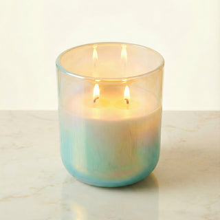 Shimmering Sea – Staycation ocean-inspired premium coconut apricot wax candle lit with dual warm flames, radiant iridescent turquoise glass vessel glowing with oceanic pearl shimmer