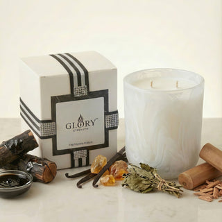 Glory Strength Light Shadow 2-wick luxury candle with gift box and fragrance notes displayed: vanilla pods, amber resin, white sage bundle, and sandalwood chips on marble