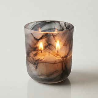Glory Strength Shadow Light 2-wick luxury candle burning inside a frosted black marbled glass vessel, warm golden flames glowing through the glass