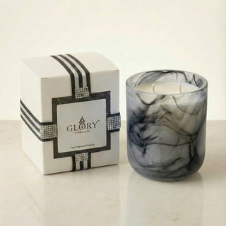 Glory Strength Shadow Light 2-wick luxury candle in a black marbled glass vessel beside its signature gift box with black stripe ribbon and rhinestone detail