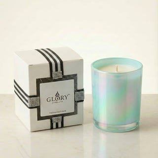 Glory Strength Shimmering Sea 8oz luxury scented candle in an iridescent turquoise glass vessel, displayed beside a white and black striped gift box with rhinestone ribbon detail on a marble surface.