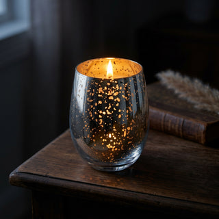 Glory Strength Today candle from the Legacy Collection — silver mercury glass vessel burning on a dark walnut table with pampas grass and leather book, warm gold flame glowing through speckled plating