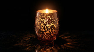 Glory Strength Yesterday candle from the Legacy Collection — rose gold mercury glass vessel lit against a dark background, flame casting warm amber light through the speckled plating